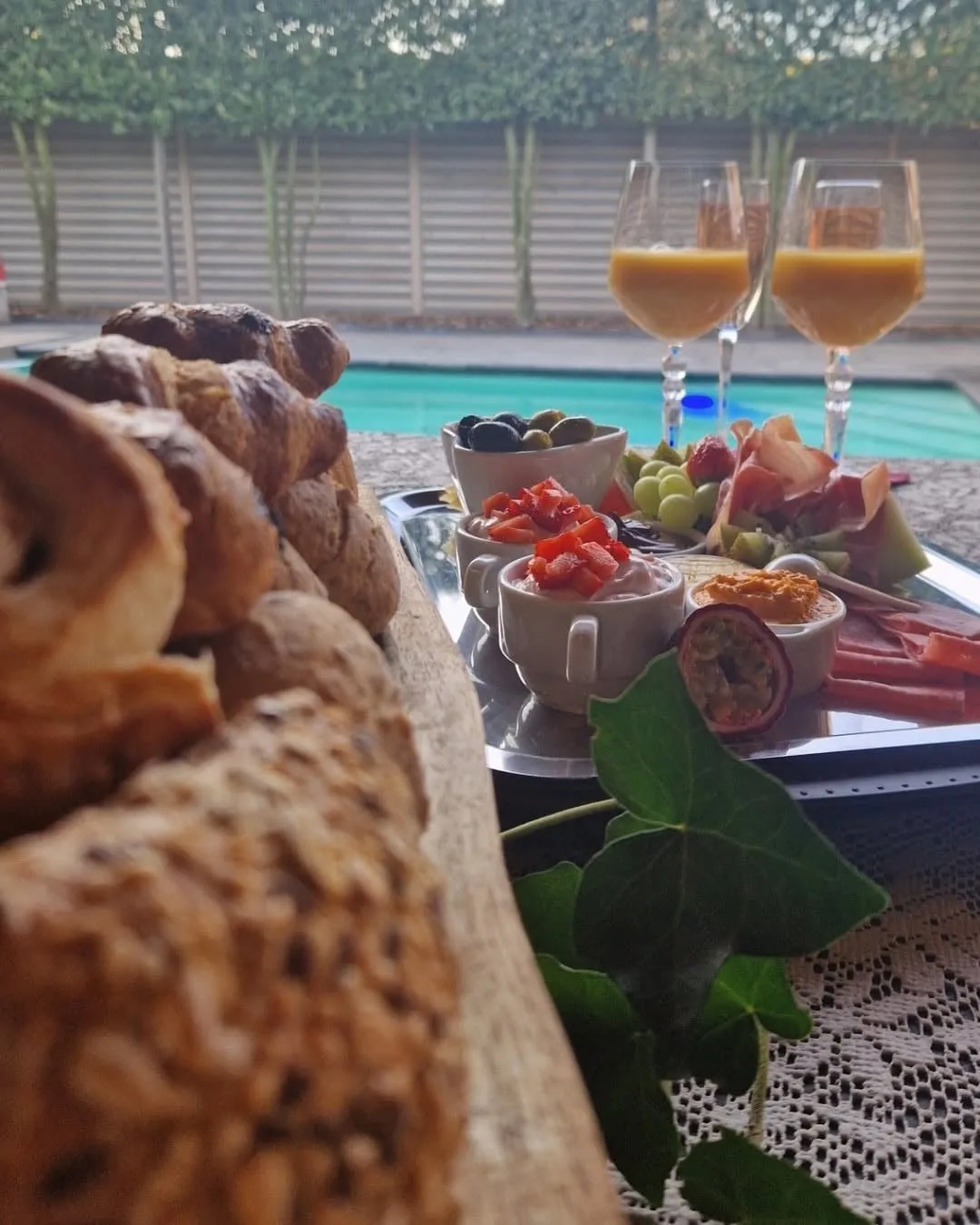 Een ontbijt met croissants, vers fruit en twee glazen aan de rand van het zwembad