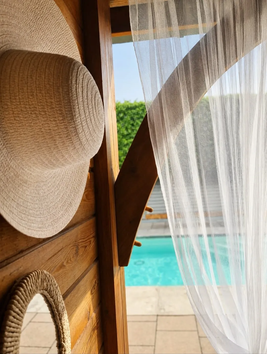 Een zomerhoed bij het wapperende gordijn van het poolhouse
